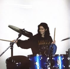 a woman playing drums in front of a white wall with blue sparkles on it