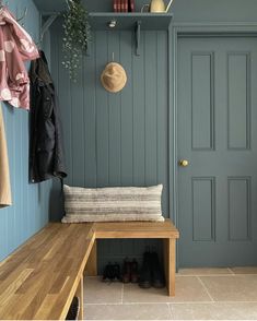 a wooden bench sitting in front of a blue wall next to a coat rack with shoes on it