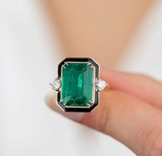 a woman's hand holding an emerald and diamond ring