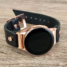 a close up of a wrist watch on a wooden table with a black leather strap