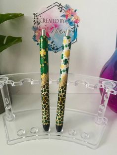 two pens sitting on top of each other in front of a clear holder with flowers