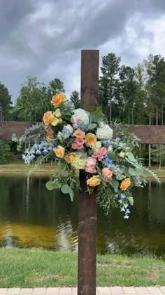 a cross decorated with flowers on the side of a lake