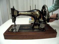 an antique sewing machine sitting on top of a wooden table next to a person's hand