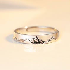 a close up of a ring on a white surface with mountains in the middle and birds flying around it