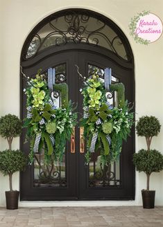 two green wreaths are on the front door of a house with potted plants