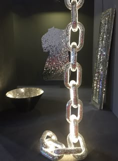 a large metal chain is on display in a room with other art pieces behind it