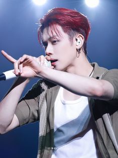 a male with red hair and piercings on his ear holding a microphone in front of him