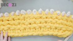 someone is crocheting a yellow and white knitted object with their hands on it