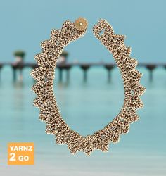 a close up of a bracelet on a beach near the ocean with a pier in the background