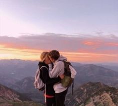 two people standing on top of a mountain kissing