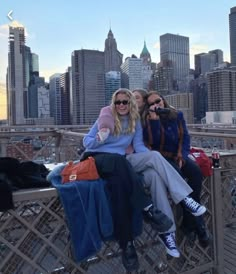 two women sitting on top of a metal fence in front of a cityscape