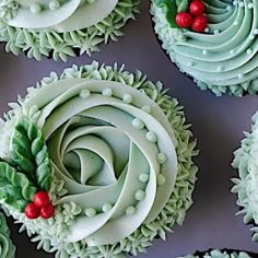 cupcakes decorated with green frosting and red berries are arranged on a table