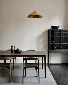 a dining room table and chairs in front of a wall with a light hanging over it