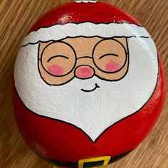 a painted rock with a santa claus face on it, sitting on a wooden surface