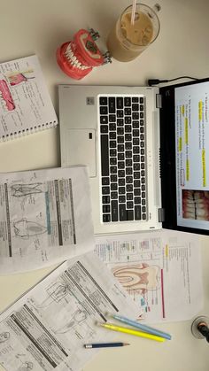 an open laptop computer sitting on top of a desk next to papers and pencils