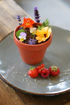 two strawberries sit on a plate next to a flower pot with flowers in it