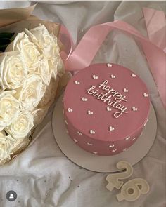 a pink birthday cake and bouquet of white roses