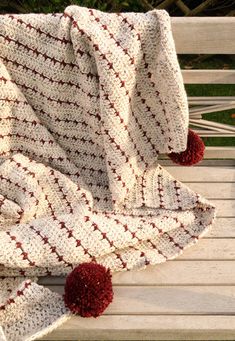 a crocheted blanket sitting on top of a wooden bench next to a red pom - pom