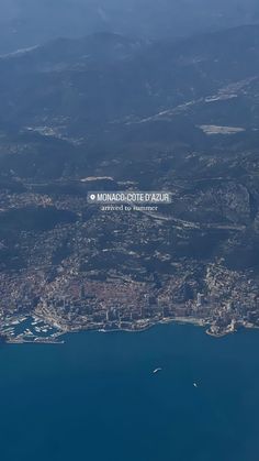 the view from an airplane looking down on a city and water area with mountains in the background