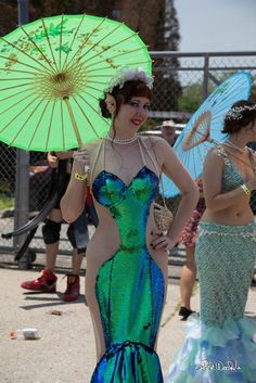 two women dressed in costumes and holding parasols at a parade, one woman is wearing a costume