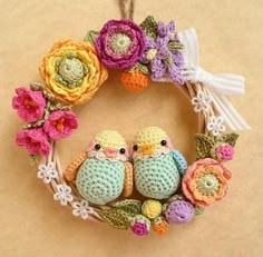 two crocheted birds sitting on a wreath with flowers and ribbons hanging from it