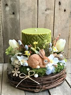 a basket filled with flowers and an easter bunny sitting next to a green lit candle