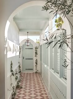 an arched hallway leading to a white door and tiled floor with potted plants on either side