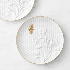 two white and gold plates with a bee on the side, one is decorated with leaves