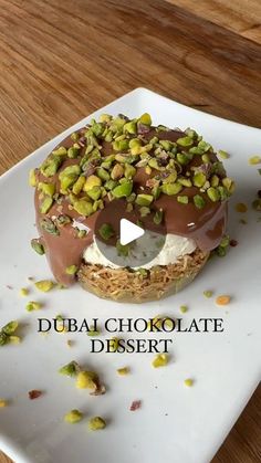 a chocolate dessert with pistachios and nuts on a white square plate that says, dubai chocolate desert