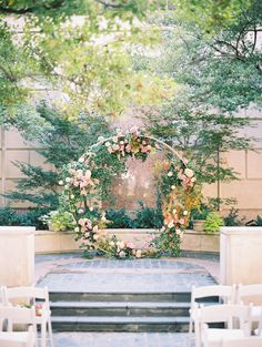 an outdoor ceremony set up with white chairs and pink flowers on the aisle, surrounded by greenery