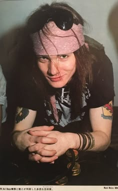 a man with long hair wearing a pink bandana and holding his hands on his chest