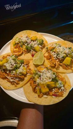 four tacos on a white plate with lime wedges and shredded parmesan cheese