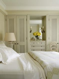 a bedroom with white furniture and yellow flowers in the vase on the dresser next to the bed