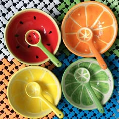 four colorful bowls with spoons and fruit slices in them sitting on a tablecloth