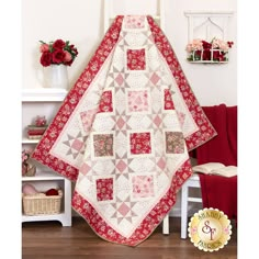 a red and white quilt hanging from the side of a wall next to a chair