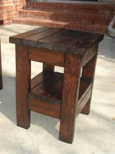 a small wooden table sitting on top of a cement floor next to a brick wall