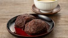 two chocolate cookies on a plate next to a cup of tea