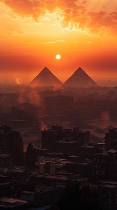 the sun is setting behind two pyramids in an orange and pink sky over a city