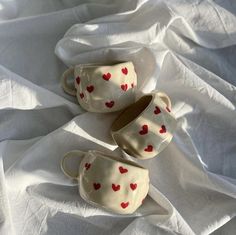 three cups with hearts painted on them are sitting on a white cloth covered tablecloth