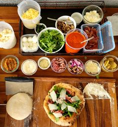 a pizza sitting on top of a wooden cutting board next to bowls of toppings