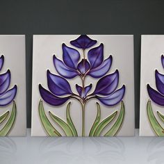 three decorative tile pieces with purple flowers on the side and green leaves on the back