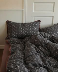 an unmade bed with black and white floral comforter on it, next to a door