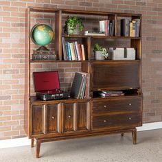 a wooden bookcase with drawers and a laptop on the top, in front of a brick wall