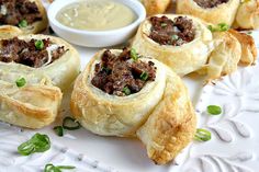 several pastries on a white plate with dipping sauce in the middle and green onions