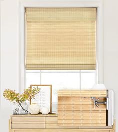 a wooden dresser topped with a vase filled with flowers next to a window covered in blinds