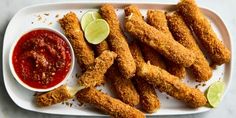 fried fish sticks on a plate with ketchup and lime wedges next to it