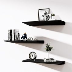 two black shelves with books and pictures on them, one shelf has a small clock