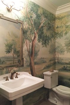 a bathroom with a painting on the wall next to a toilet, sink and mirror