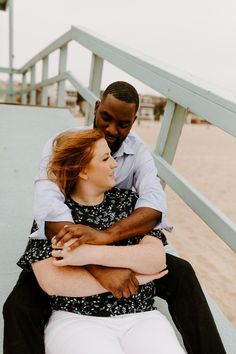 a man and woman are sitting on the steps at the beach, hugging each other