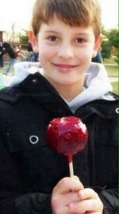 a young boy holding an apple lollipop in his hand